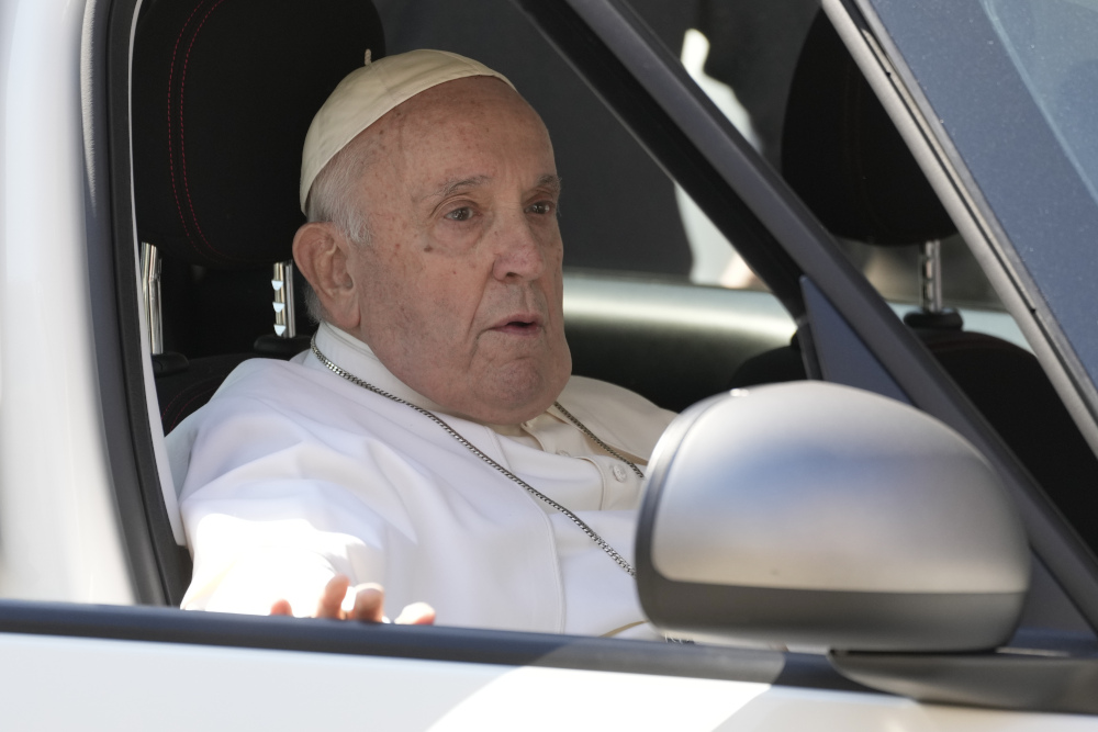 Pope Francis sits in a car with his hand on the door and his mouth slightly open