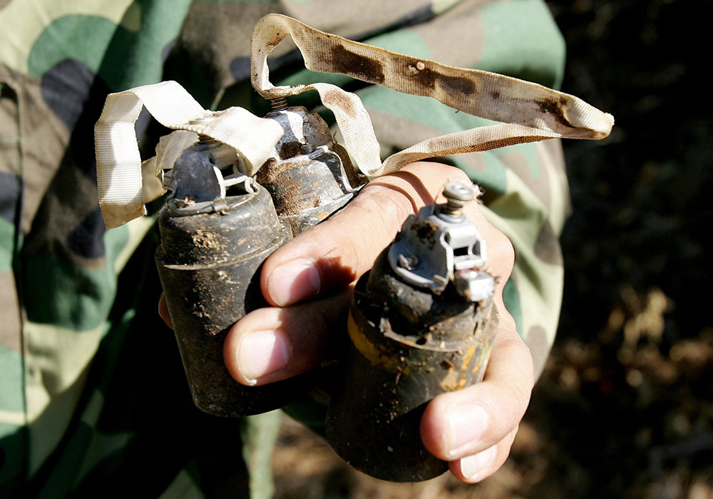 A member of a U.N. mine-clearing unit carries unexploded bomblets from cluster bombs in this Sept. 5, 2006, file photo. These cluster bombs were dropped in Lebanon by Israeli forces during their conflict with Hezbollah in the summer of 2006. (CNS/Reuters/Peter Andrews)