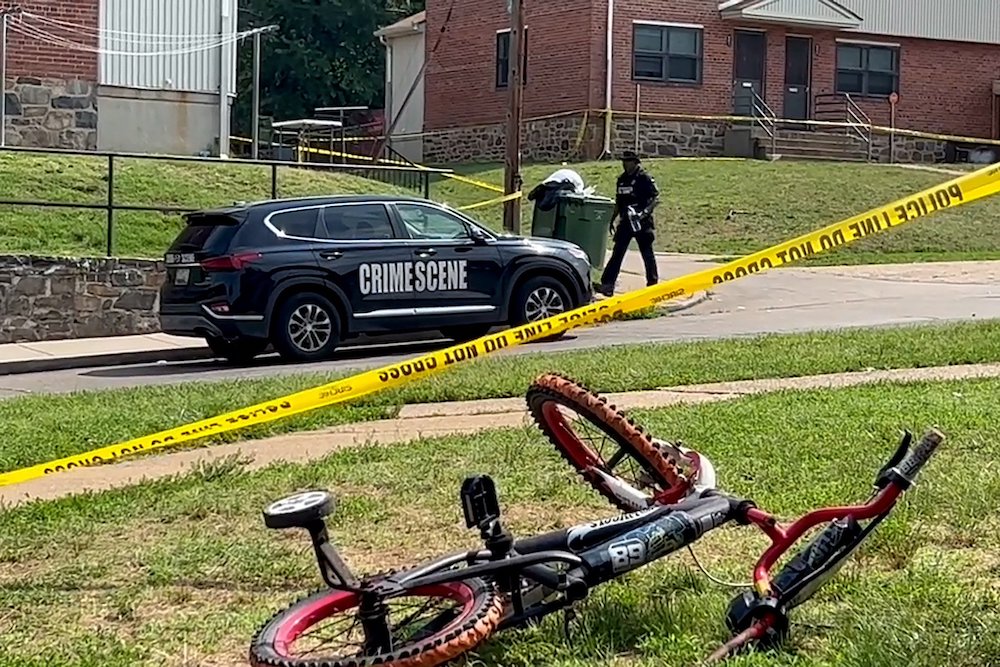 A child's bicycle, seen in a still image from video, lies on a lawn as a police officer walks down a residential street in Baltimore July 2, after a mass shooting at a Fourth of July holiday weekend block party. (OSV News/Reuters)