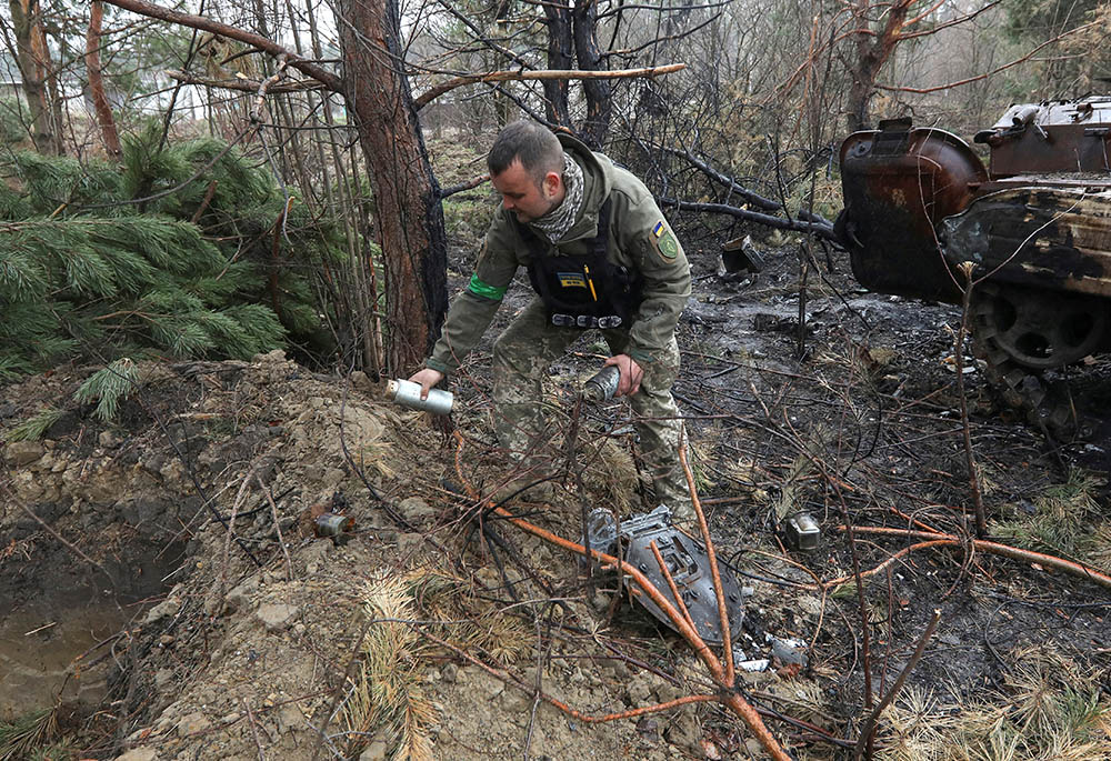 A Ukrainian soldier picks up unexploded parts of a cluster bomb left after Russia's invasion near the village of Motyzhyn, Ukraine, April 10, 2022. (OSV News/Reuters/Mykola Tymchenko)