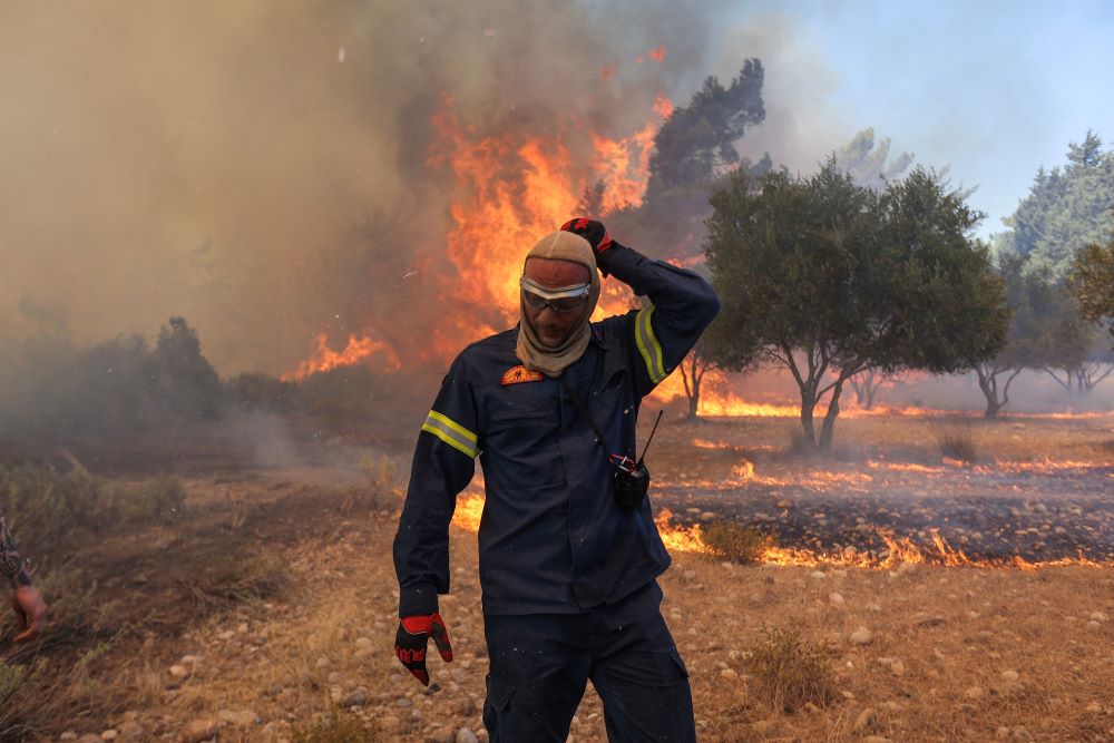 A firefighter walks next to rising flames as a wildfire burns near the village of Vati, on the island of Rhodes, Greece, July 25, 2023. (OSV News/Reuters/Nicolas Economou)