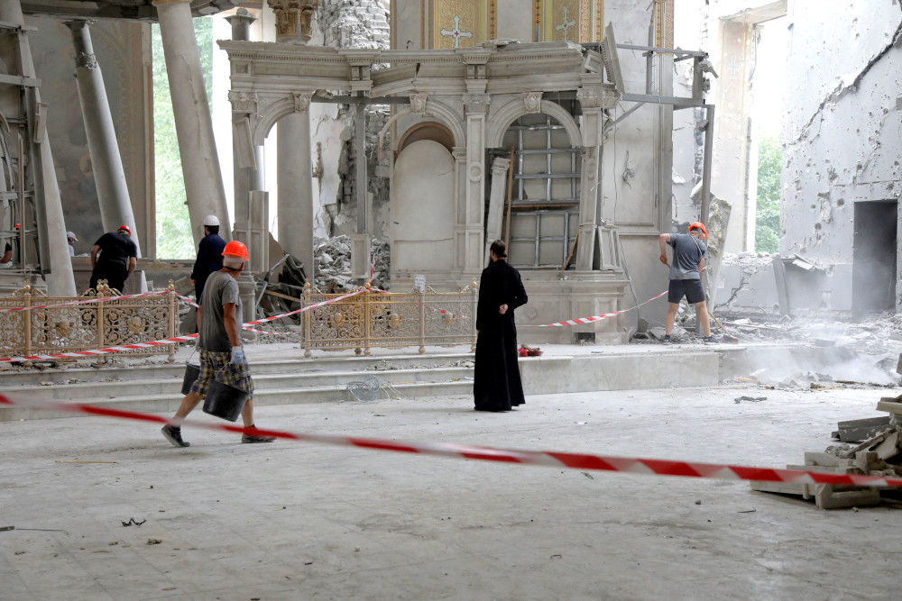 A person in all black and a construction worker stand in a crumbling cathedral