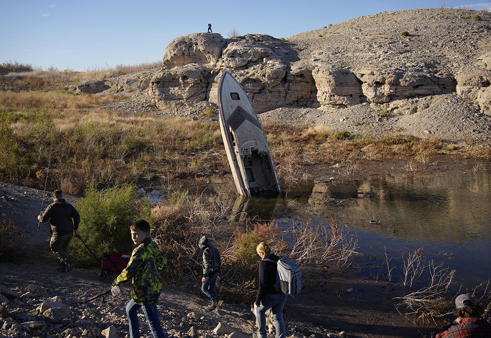People walk by a formerly sunken boat standing upright into the air with its stern buried in the mud along the shoreline of the drought-stricken Lake Mead at the Lake Mead National Recreation Area on Jan. 27 near Boulder City, Nevada. (AP/John Locher, File)