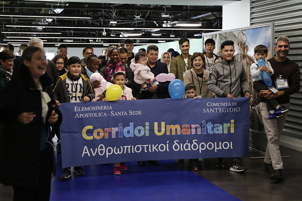 Refugees hold a banner reading "Humanitarian Corridors" in Italian and Greek upon their arrival at Fiumicino airport, Wednesday, Dec. 4, 2019. Thirty-three refugees coming from Afghanistan, Cameroon and Togo arrived in Rome from the Greek island of Lesbos, thanks to Sant'Egidio's "Humanitarian Corridors" project. (AP/Alessandra Tarantino)