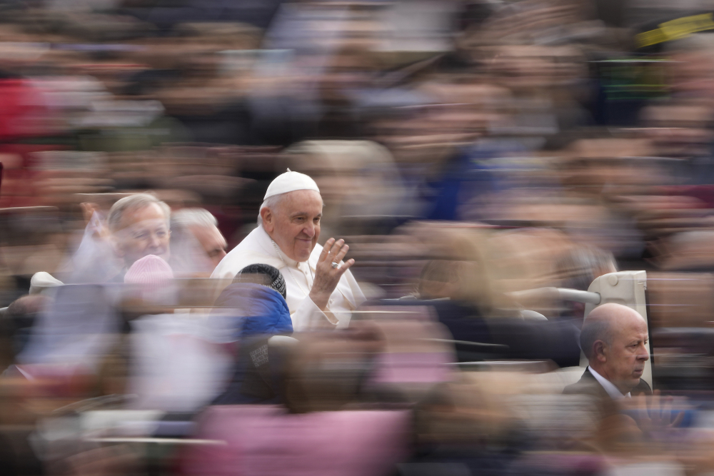 Pope Francis smiles and waves as he rides through a blurred out crowd of people