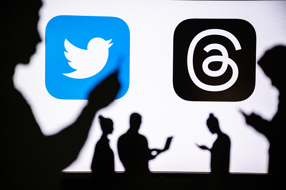 Silhouettes of people looking at devices with the logos of Twitter and Threads behind them (Dreamstime/Peter Kováč)