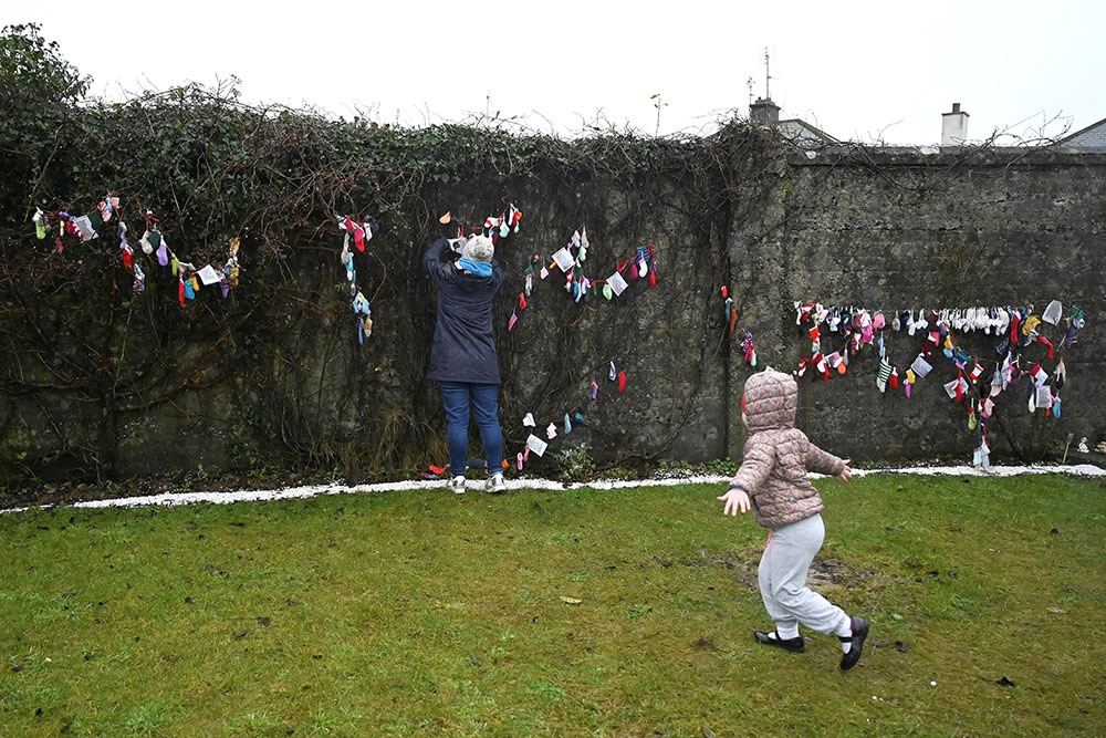 Denise Gormley and her 7-year-old daughter, Rosa, pay their respects at a cemetery in Tuam, Ireland, where the bodies of nearly 800 infants were uncovered at the site of a former Catholic home for unmarried mothers and their children. The photo was taken Jan. 12, 2021, the day a commission investigating the treatment of women in such homes released its report. (CNS/Reuters/Clodagh Kilcoyne)
