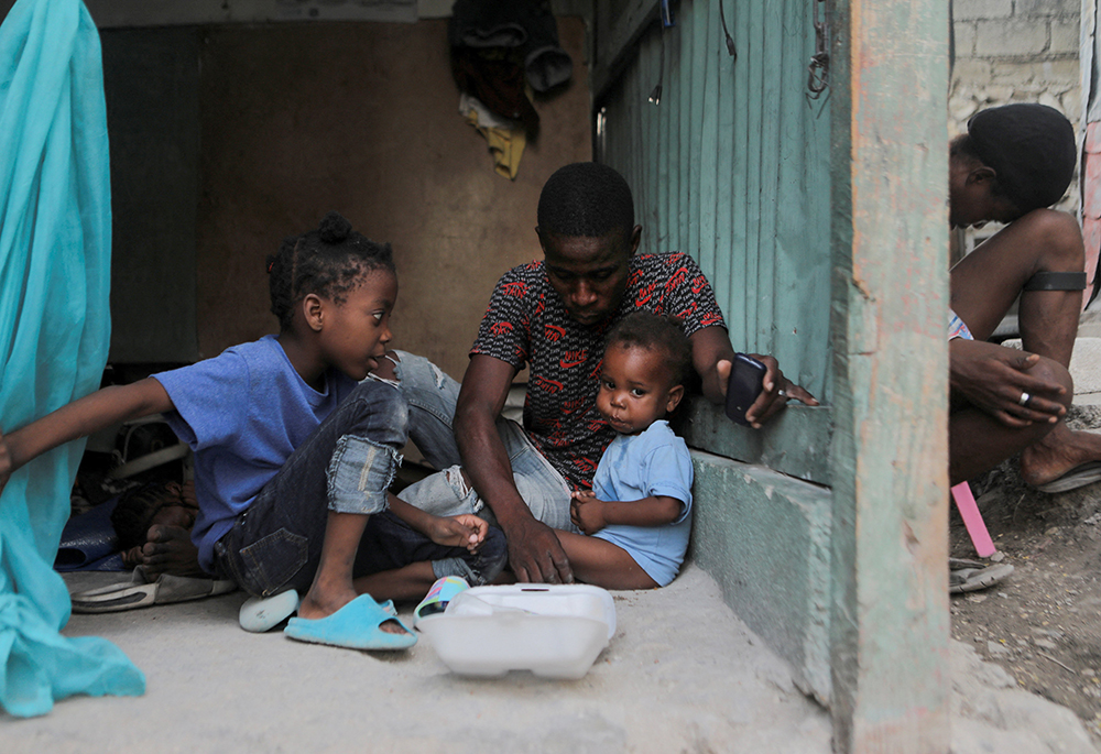 Una familia comparte una comida en el campamento de refugiados de la Nueva Iglesia de Dios de la Liberación, el 19 de junio en Puerto Príncipe, Haití. El campamento alberga ahora a 120 familias de diversos barrios que se han visto muy afectados desde que las bandas ampliaron su territorio y ahora controlan comunidades en las que viven unos 2 millones de personas. (Foto: OSV News/Reuters/Ralph Tedy Erol)