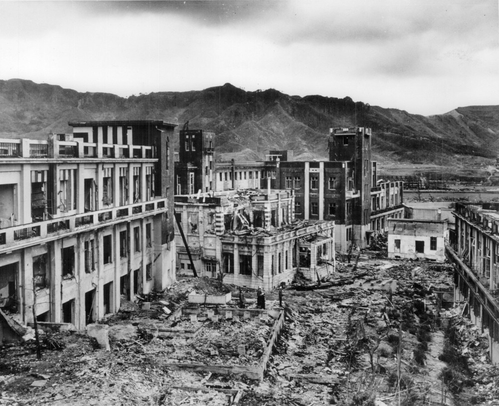 A black and white photo of the ruins of buildings. Some are in rubble and some are still standing.