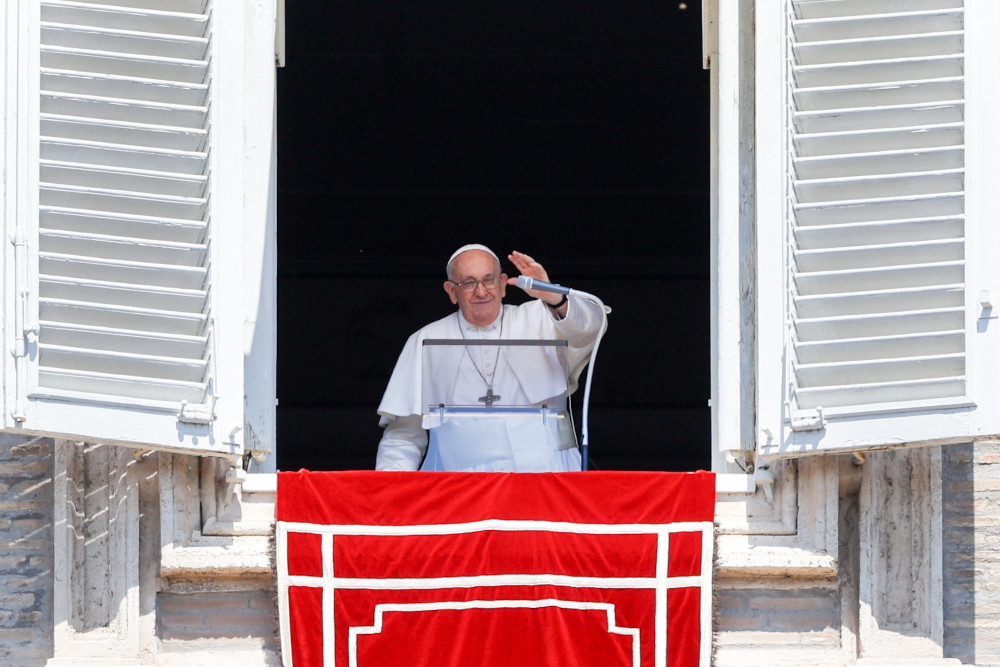 Pope Francis raises his hand while standing in his apartment window