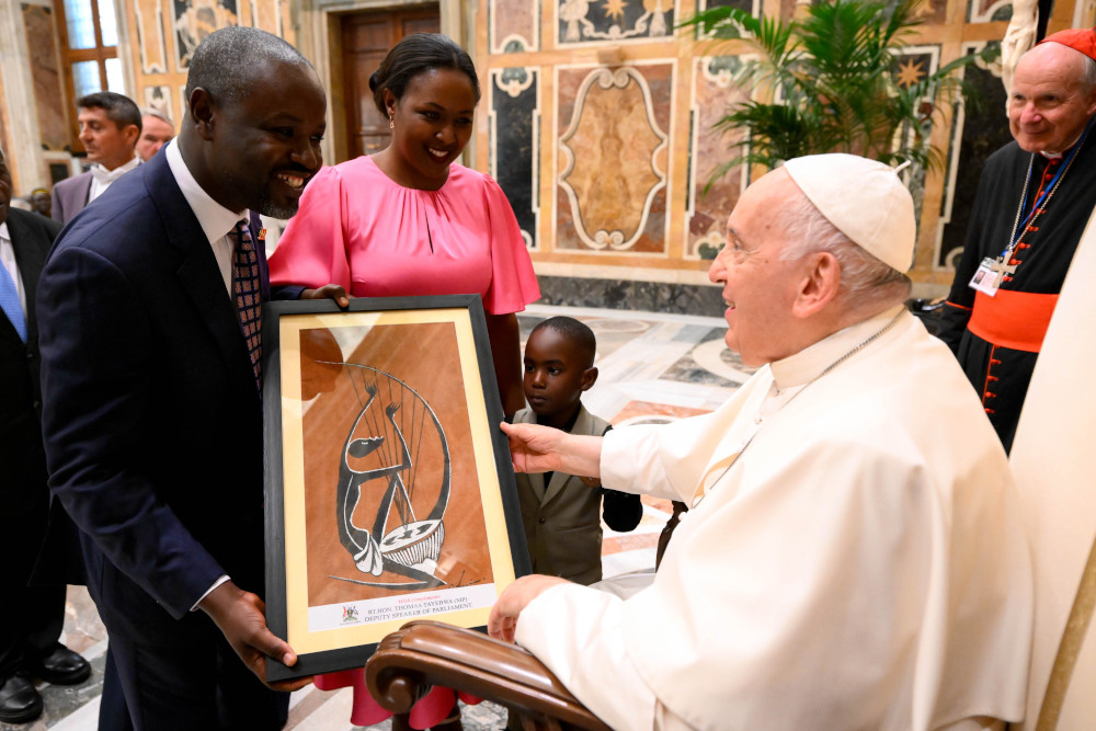 A Black man wearing a suit hands an an African painting of a musician to Pope Francis