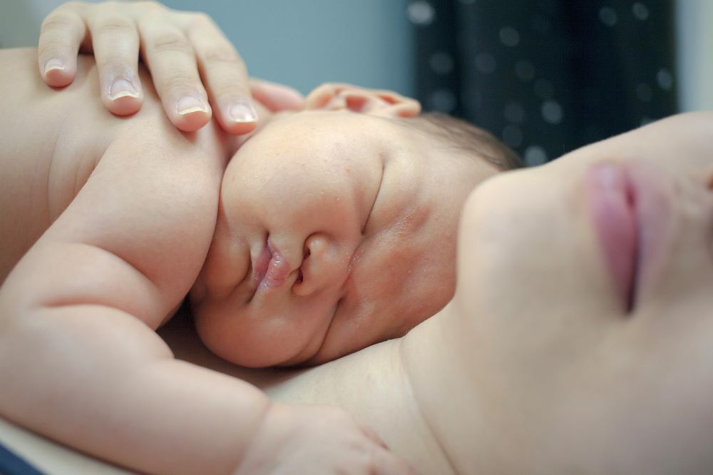 Woman hugs baby on her chest.