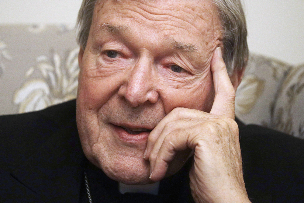 An older white man wearing a clerical collar has his pointer finger on his forehead as his other fingers rest on his cheek