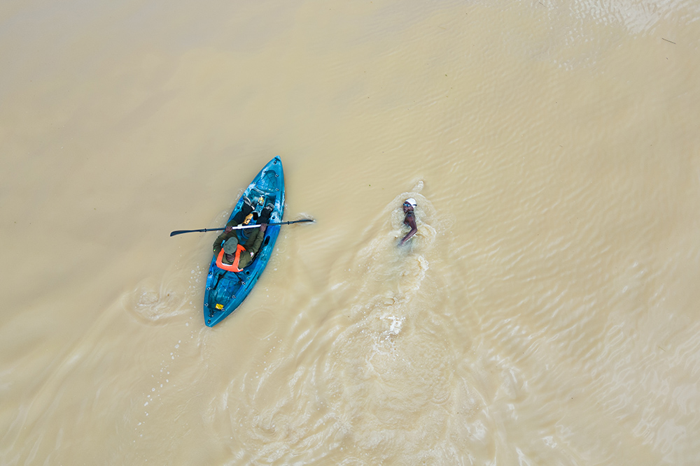 A member of the Agbetsi Living Water Swim expedition crew rides along while Yvette Tetteh swims in the Volta River. (Courtesy of the Or Foundation)