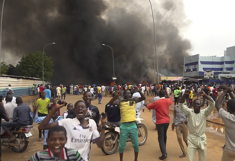 With the headquarters of the ruling party burning in the back, supporters of Niger's ruling junta demonstrate July 27 in Niamey, Niger. Defense chiefs from the West African regional bloc, ECOWAS, were to meet Aug. 17 in Ghana to discuss Niger's crisis after a deadline passed for mutinous soldiers to release and reinstate President Mohamed Bazoum or face military intervention. (AP photo/Fatahoulaye Hassane Midou, file)