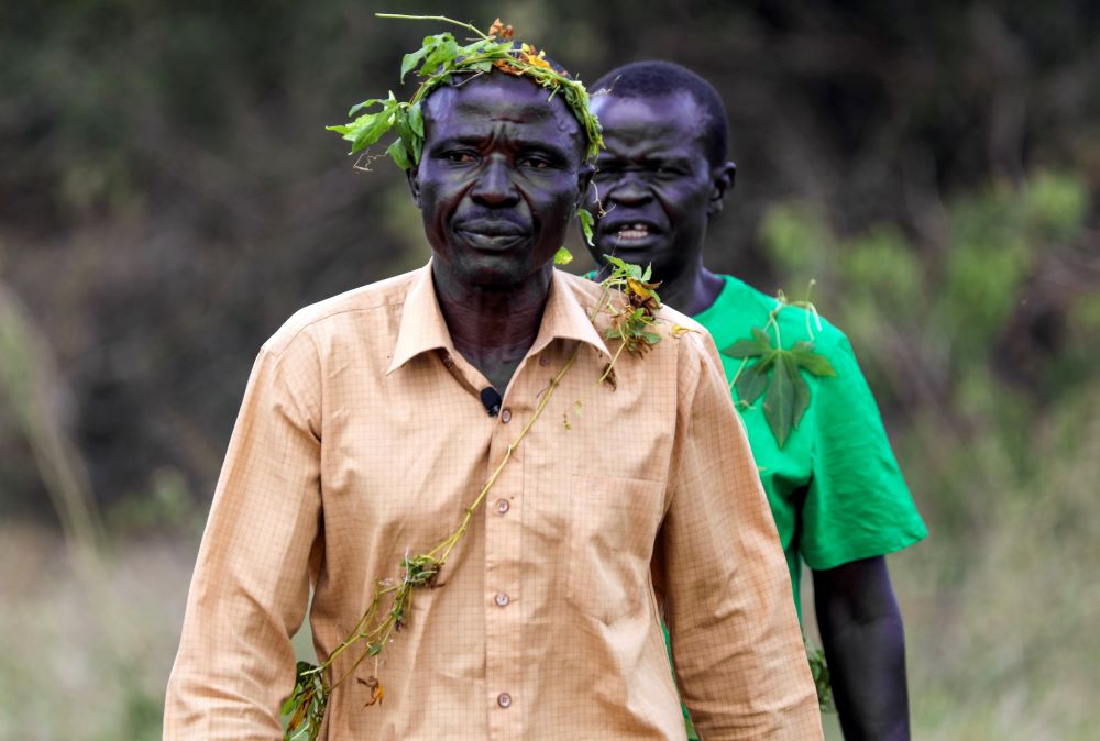 John Gafabusa, followed by Abiri Ntarwete, walks from the Mutyona natural sacred site near Buliisa, Uganda, Aug. 3, 2023.