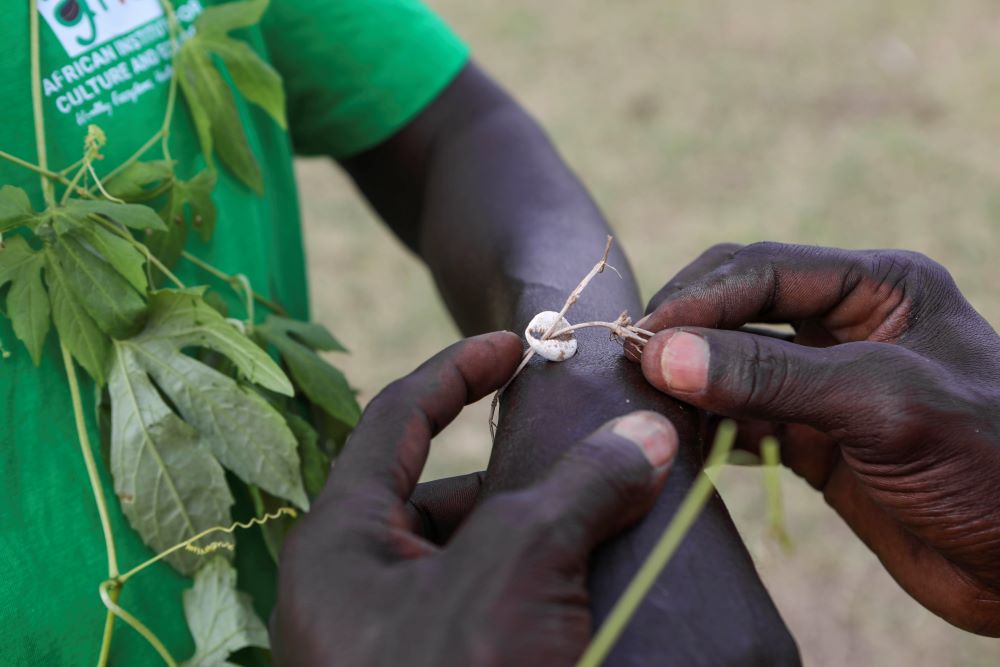 John Gafabusa ties a cowrie shell on Abiri Ntarwete's arm before visiting the Mutyona natural sacred near Buliisa, Uganda, Aug. 3, 2023.