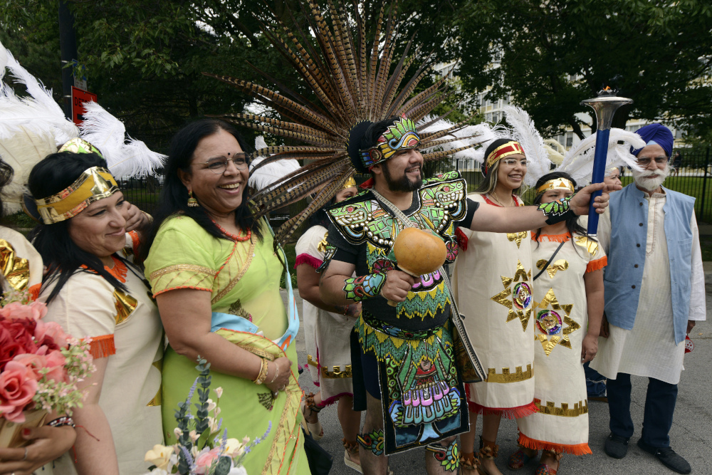 Brown people wearing feather headdresses stand next to a brown woman wearing a bindi and a brown man wearing a turban