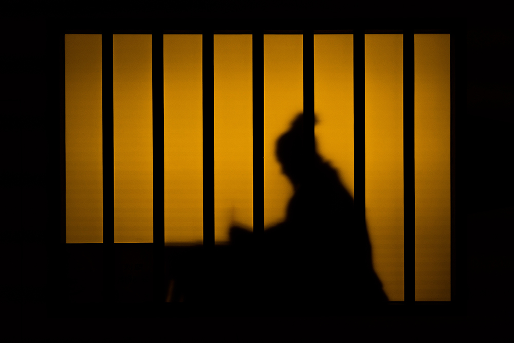 The silhouette of a person behind prison bars (Unsplash/Akira)