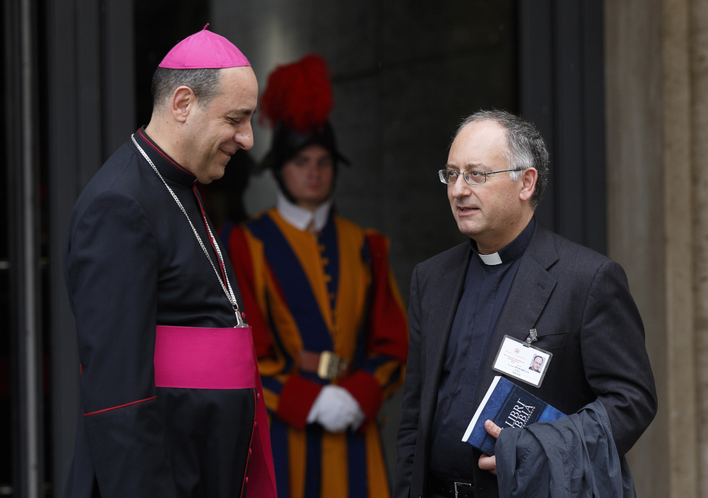 A man wearing bishop's clothes talks to a man wearing a clerical collar. A Swiss guard is visible in the background.