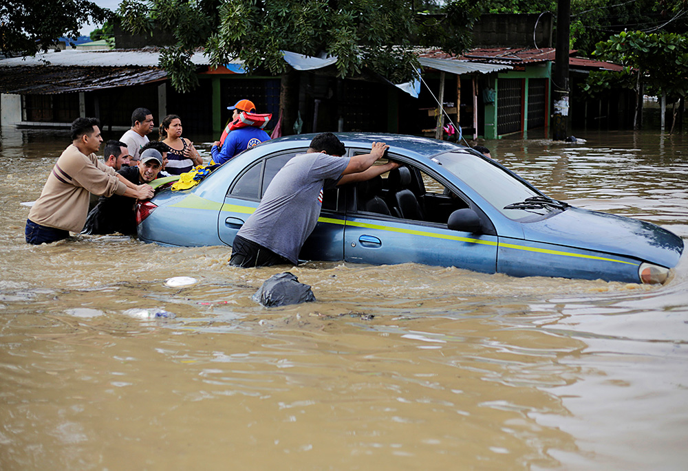 Men push a car through floodwaters in La Lima, Honduras, Nov. 5, 2020, in the rain-heavy remains of Hurricane Eta. (CNS/Reuters/Jorge Cabrera)