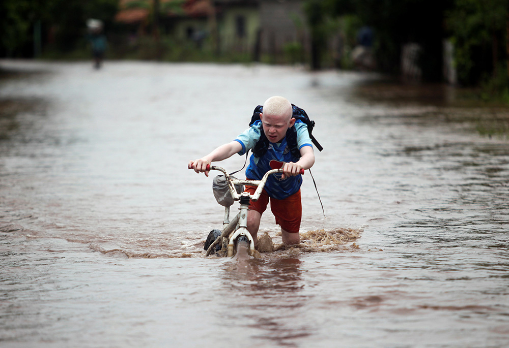 A child pushes his bicycle through a flooded road in Marcovia, Honduras, Nov. 18, 2020, after the passing of Hurricane Iota. (CNS/Reuters/Jorge Cabrera)