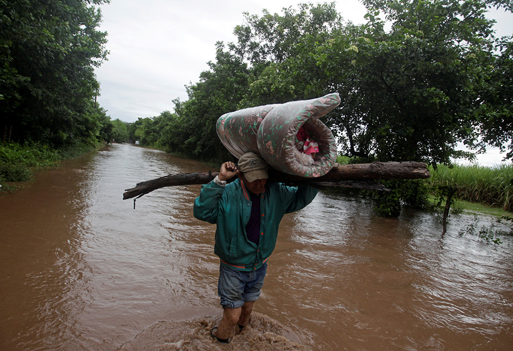 A man carries his belongings through a flooded road in Marcovia, Honduras, Nov. 18, 2020, after the passing of Hurricane Iota. (CNS/Reuters/Jorge Cabrera)