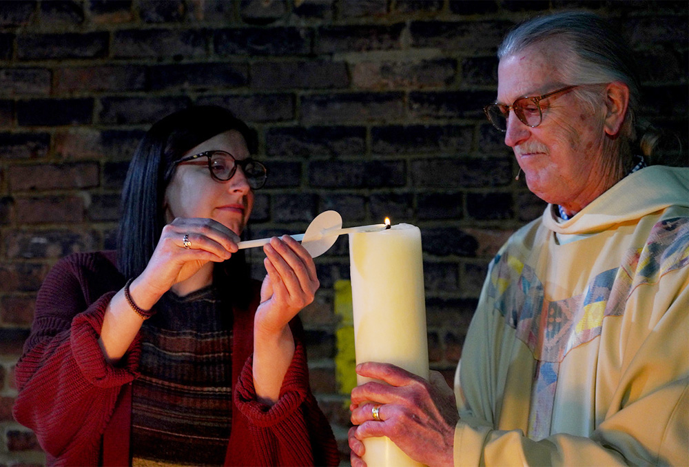 Pastoral minister Martha Ligas lights the paschal candle with "new fire" during the 2023 Easter Vigil at the Community of St. Peter in Cleveland. Pastor and administrator Bob Kloos holds the candle. (Peggy Turbett)