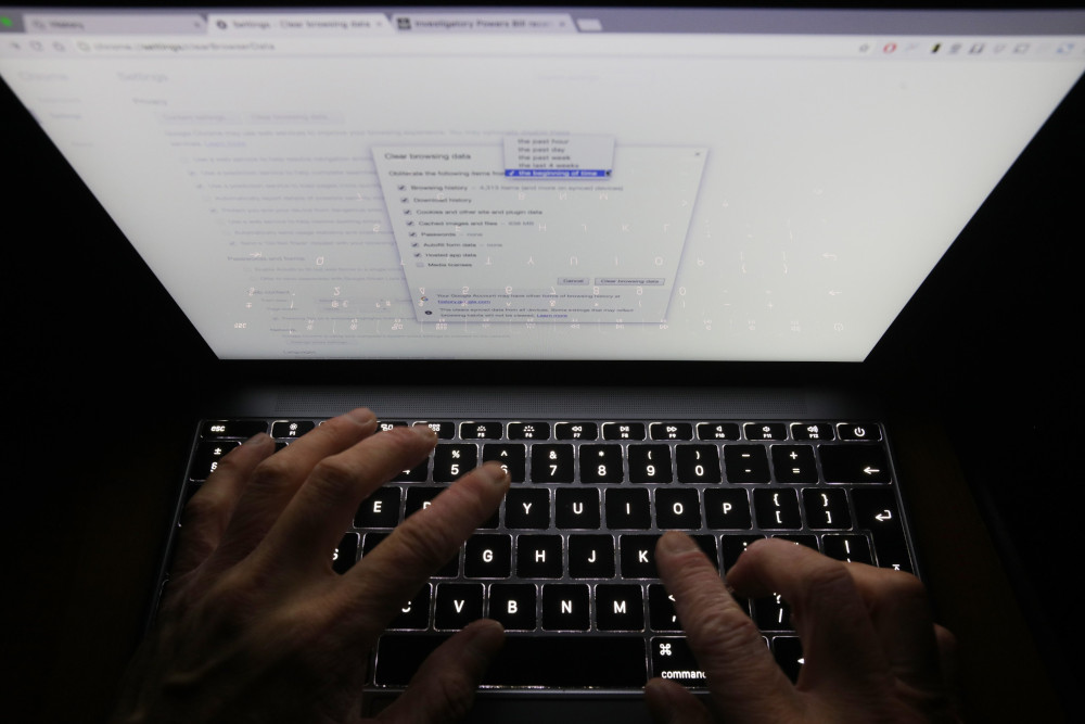 A person's fingers are visible on the keyboard of a laptop while a search is being entered on the screen