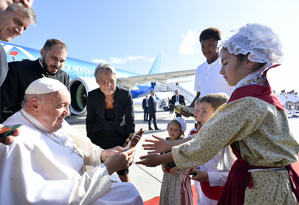 Four children and a young man give Pope Francis gifts while French Prime Minister Élisabeth Borne looks on during a brief welcoming ceremony at Marseille International Airport Sept. 22 in Marseille, France. (CNS/Vatican Media)