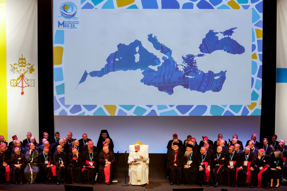 Pope sits with bishops in front of a large map of the Mediterranean region.