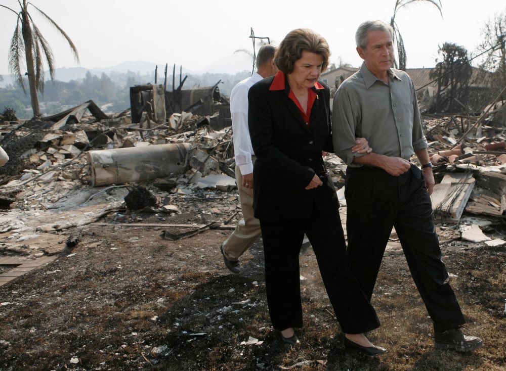 Walking arm-in-arm amid the rubble, then-U.S. President George W. Bush, and Sen. Dianne Feinstein, D-Calif., tour a San Diego neighborhood destroyed by wildfires in 2007.