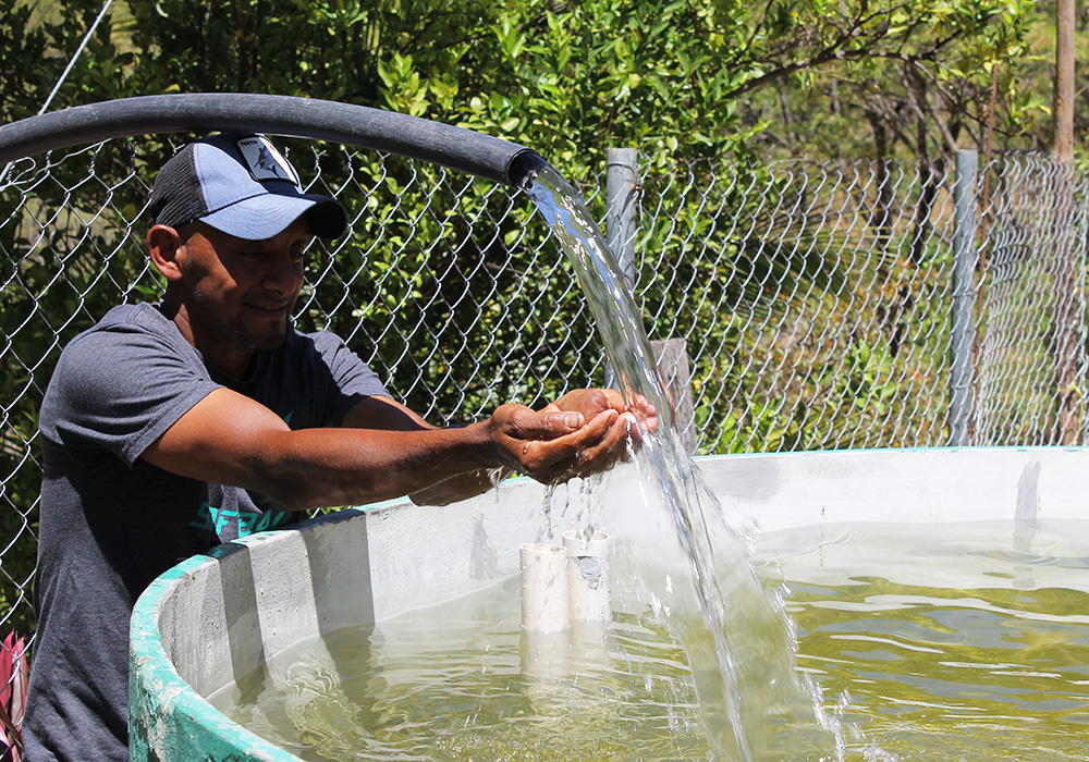 Rony Figueroa is pictured next to an 8,000 liter water harvesting tank he uses for irrigation. With the help of Catholic Relief Services, water access is less of a challenge at Figueroa's farm in central Honduras' Dry Corridor. (NCR photo/Brian Roewe)