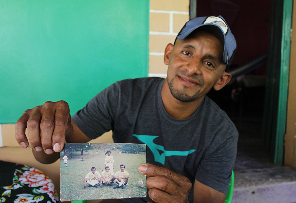 Honduran farmer Rony Figueroa holds a photo of himself as a child playing soccer with adults, including his dad, on a soccer field on the Figueroa family property. Figueroa recalls during his childhood the field was full of young people playing the sport every afternoon. Now it mostly lays empty. (NCR photo/Brian Roewe)