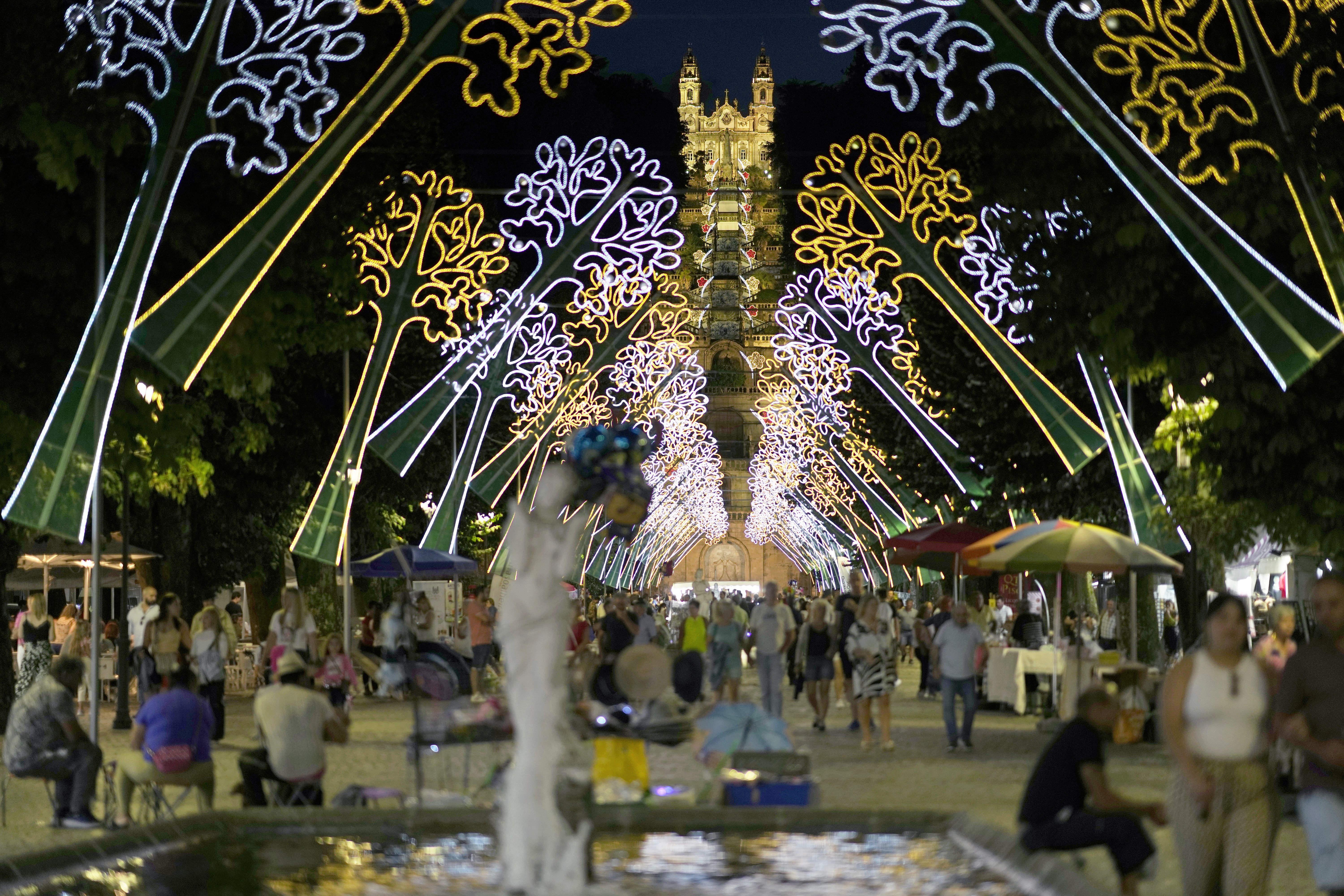 The Our Lady of Remedies Baroque sanctuary, nearly 700 steps up a monumental stone stairway, is lit in the background as people stroll along the main avenue in the small town of Lamego, in the Douro River Valley, Portugal, Friday, Sept. 8, 2023. One of Portugal's largest and oldest religious festivals, the two-week Our Lady of Remedies celebrations that culminate with a procession through the town, draw thousands. (AP Photo/Armando Franca)