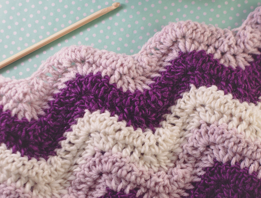 Pink, purple and white afghan blanket with a crocheting needle (Dreamstime/Jessicacasetorres)