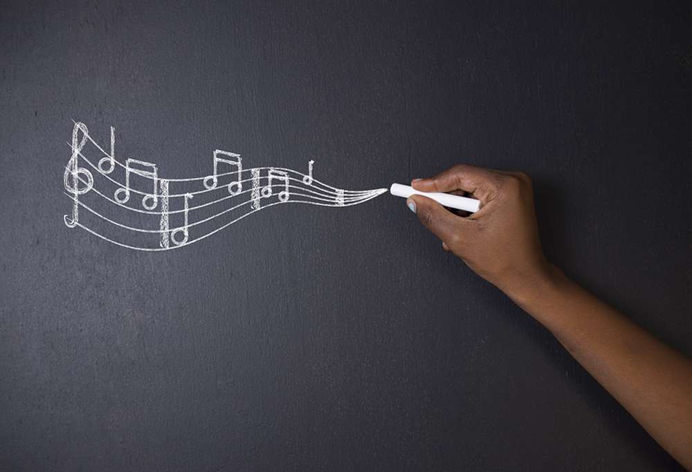 The hand of a Black person writes a bar of music in chalk on a blackboard (Dreamstime/Africa Rising Agency)