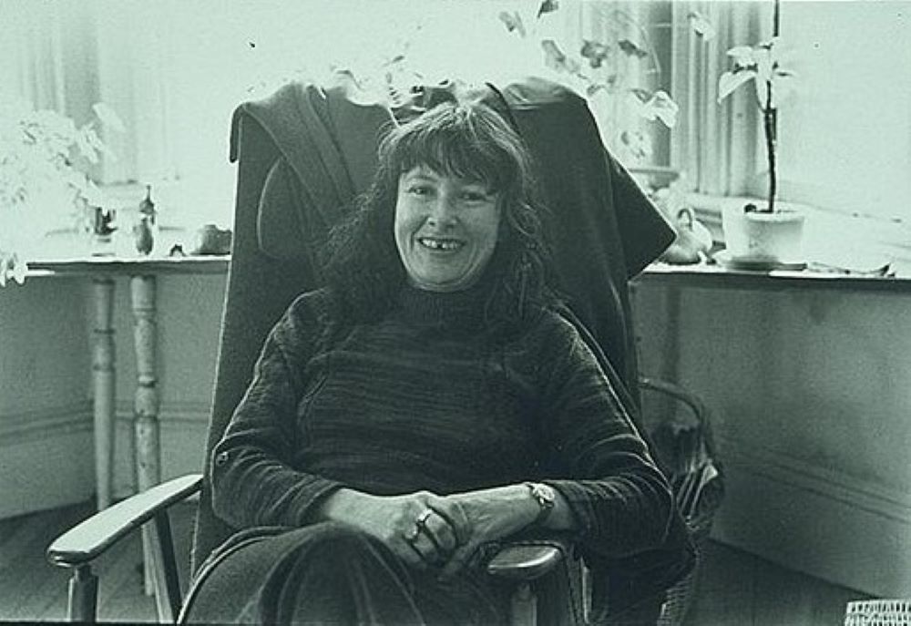 Denise Levertov sits in a chair in front of a window.