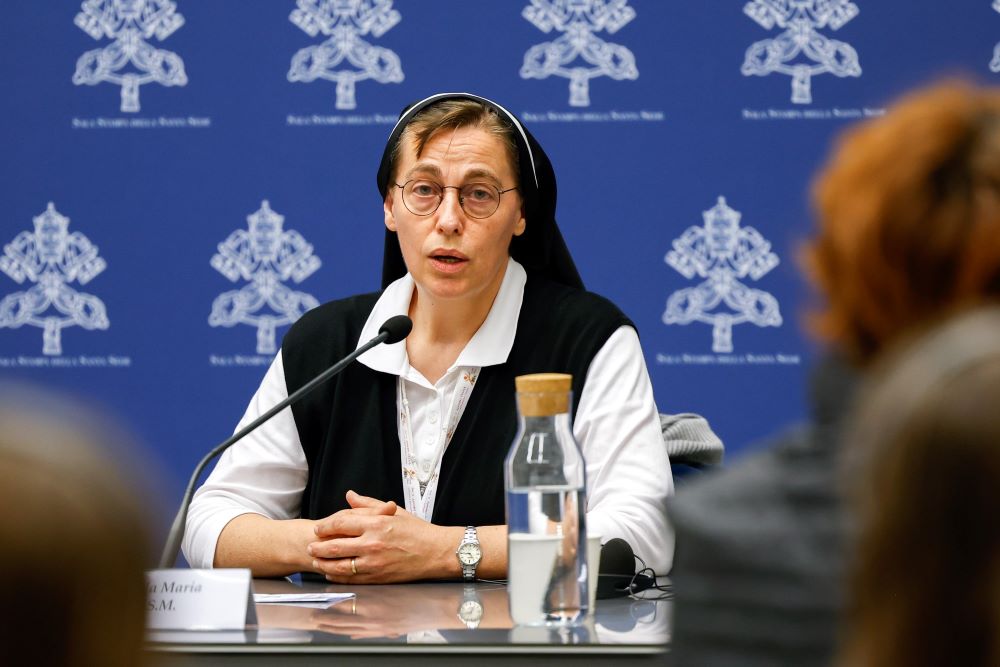 Nun sits at table and talks to group facing her,