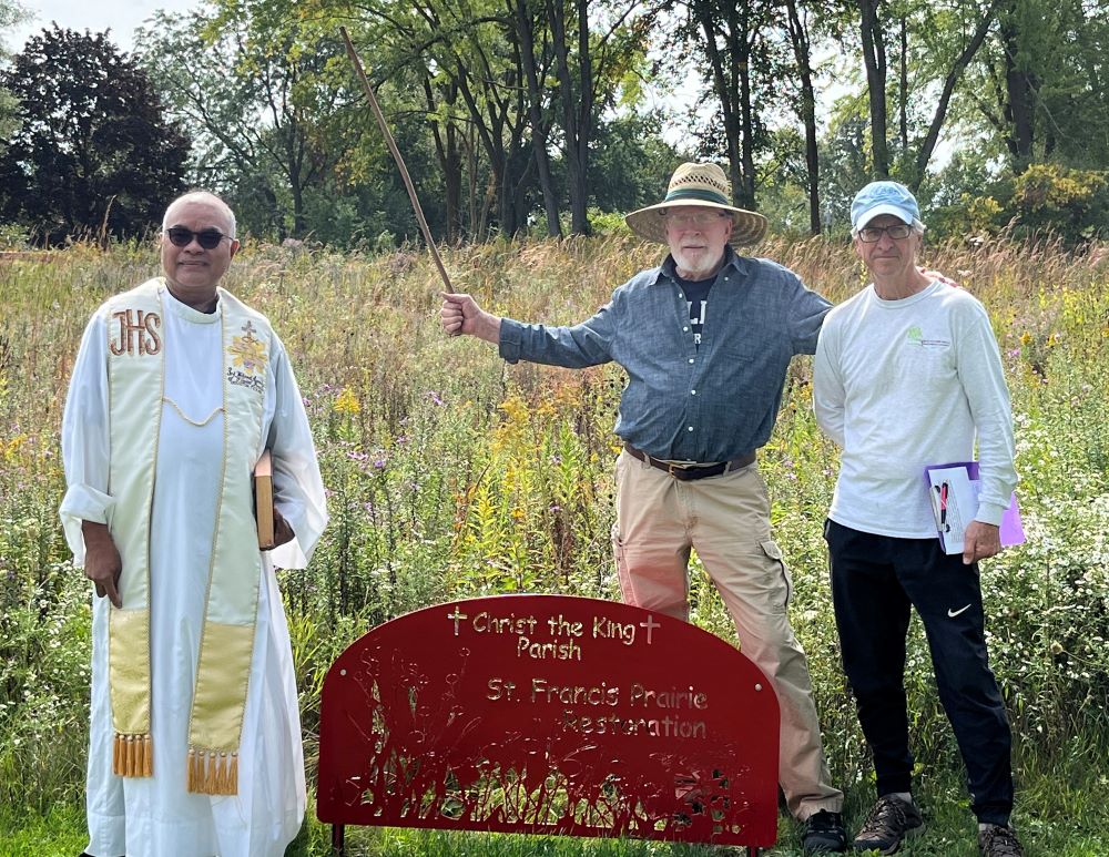 Priest stands in field with two other men.