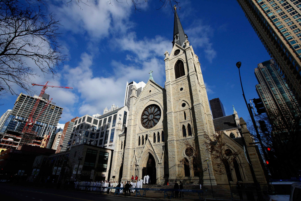 A Cathedral and its spire stretches into the sky with other high rises surrounding it