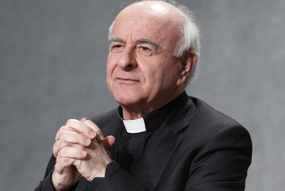 An older white man with white hair wearing a clerical collar folds his hands before his chest