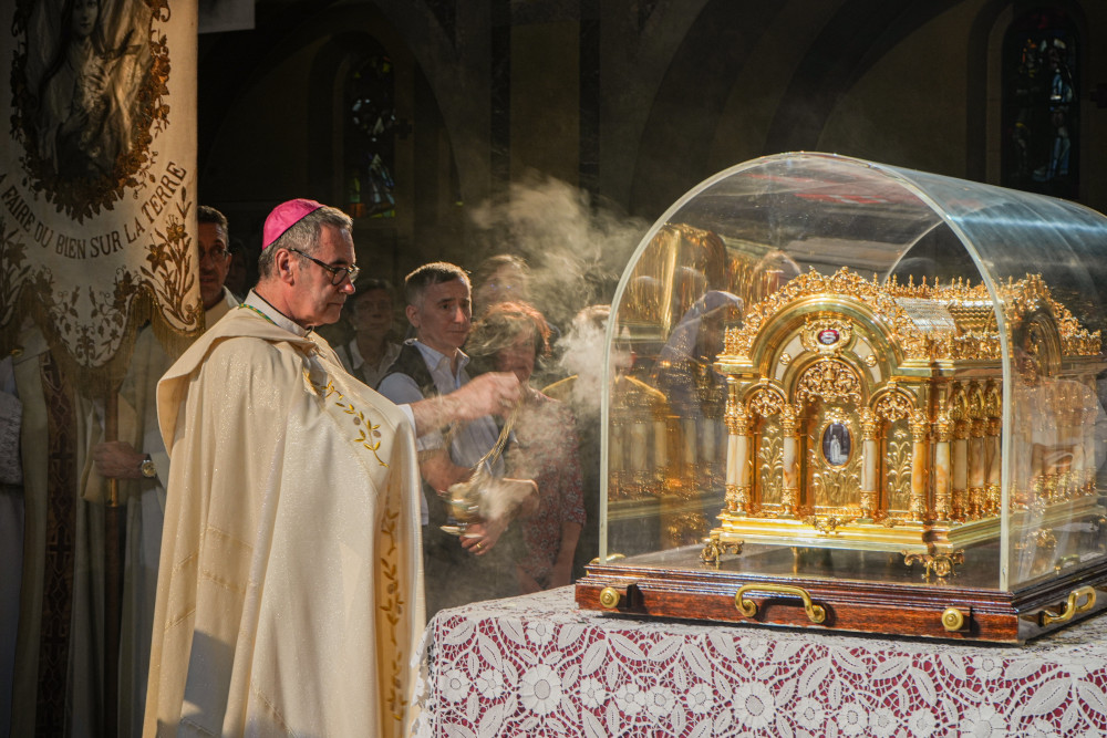A man wearing a pink zucchetto and white vestments swings incense at an ornate golden container