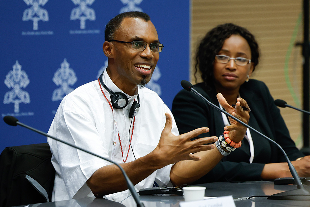 Jesuit Fr. Agbonkhianmeghe Orobator, dean of the Jesuit School of Theology at Santa Clara University in California, speaks during a briefing about the assembly of the Synod of Bishops at the Vatican Oct. 17. Sheila Leocádia Pires, secretary of the synod's information commission, looks on. (CNS/Lola Gomez)