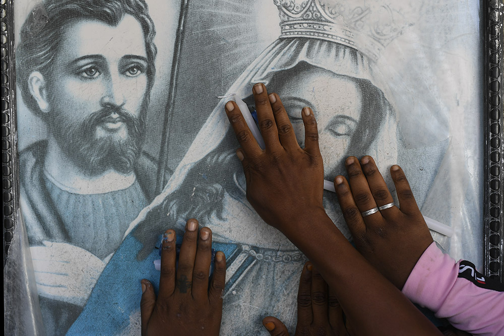 Vodou pilgrims place their hands on an image of Our Lady of Mount Carmel before the start of a Mass marking her feast day at the Mount Carmel Church in Saut d'Eau, Haiti, on July 16, 2021. The devotion plays a role in both Catholic and Vodou spirituality. (AP/Matias Delacroix)