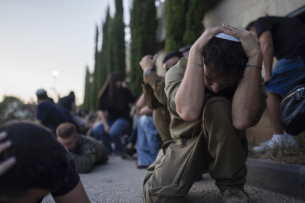 At a cemetery in Holon, central Israel, Oct. 26, Israelis take cover as a siren warns of incoming rockets fired from the Gaza Strip, during the funeral of Israeli man Sagiv Ben Svi, killed by Hamas militants while attending a music festival on Oct. 7. (AP/Petros Giannakouris)