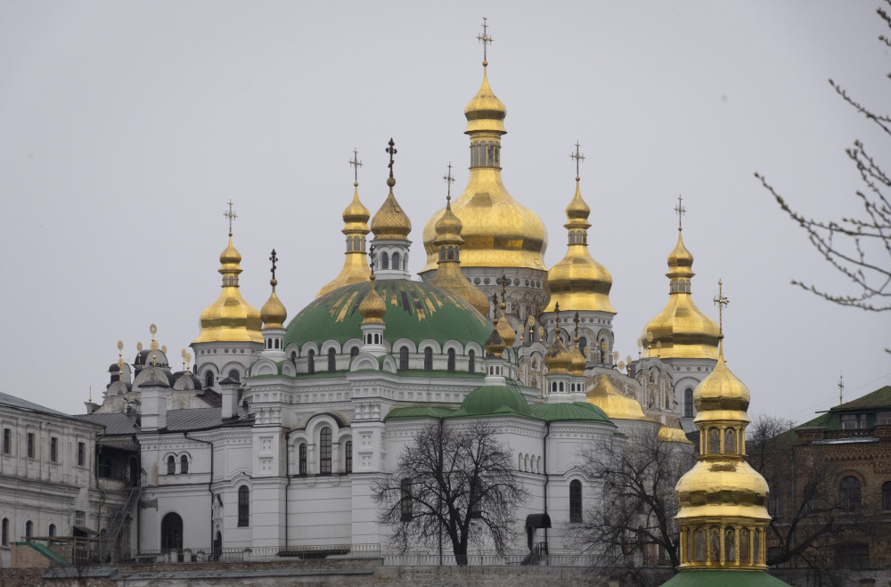 A white stone church with green domes topped with golden spires and crosses