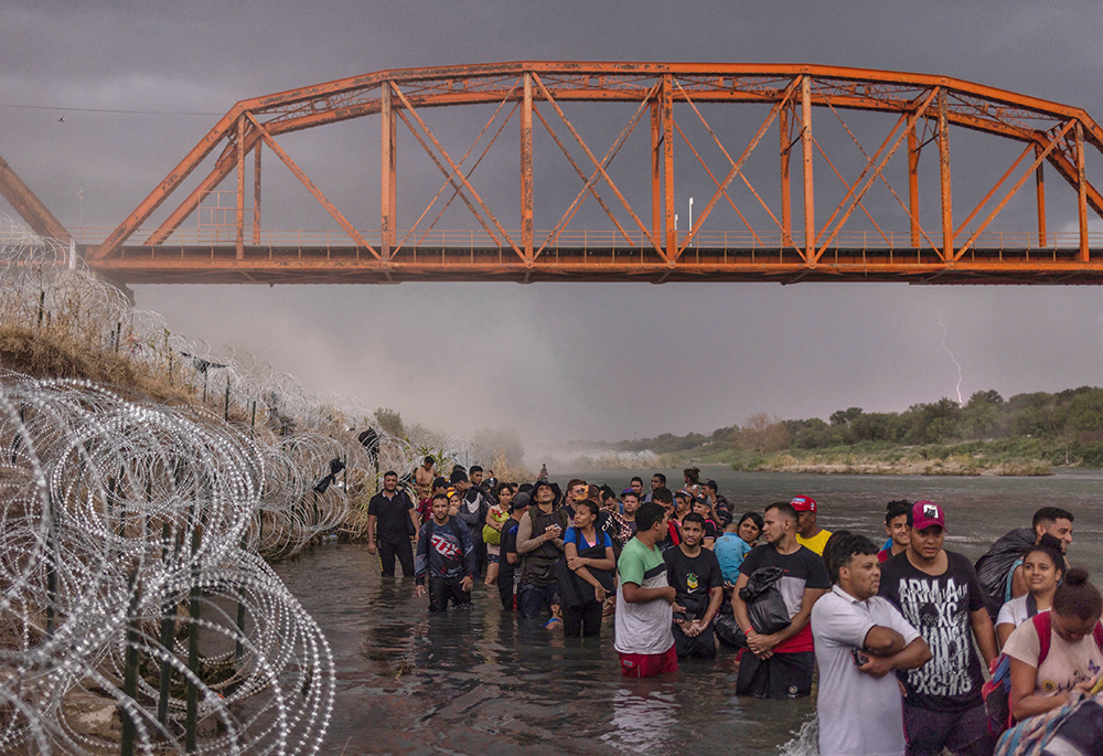 Migrantes hacen cola bajo el Puente Negro, vía del ferrocarril. Caen relámpagos y se levanta polvo durante una tormenta eléctrica, el 15 de septiembre, mientras cientos de migrantes hacen cola bajo el Puente Negro, vía del ferrocarril, y esperan a entregarse a las autoridades tras cruzar el Río Grande desde México para entrar en Estados Unidos en Eagle Pass, Texas. (Foto: OSV News/Reuters/Adrees Latif)