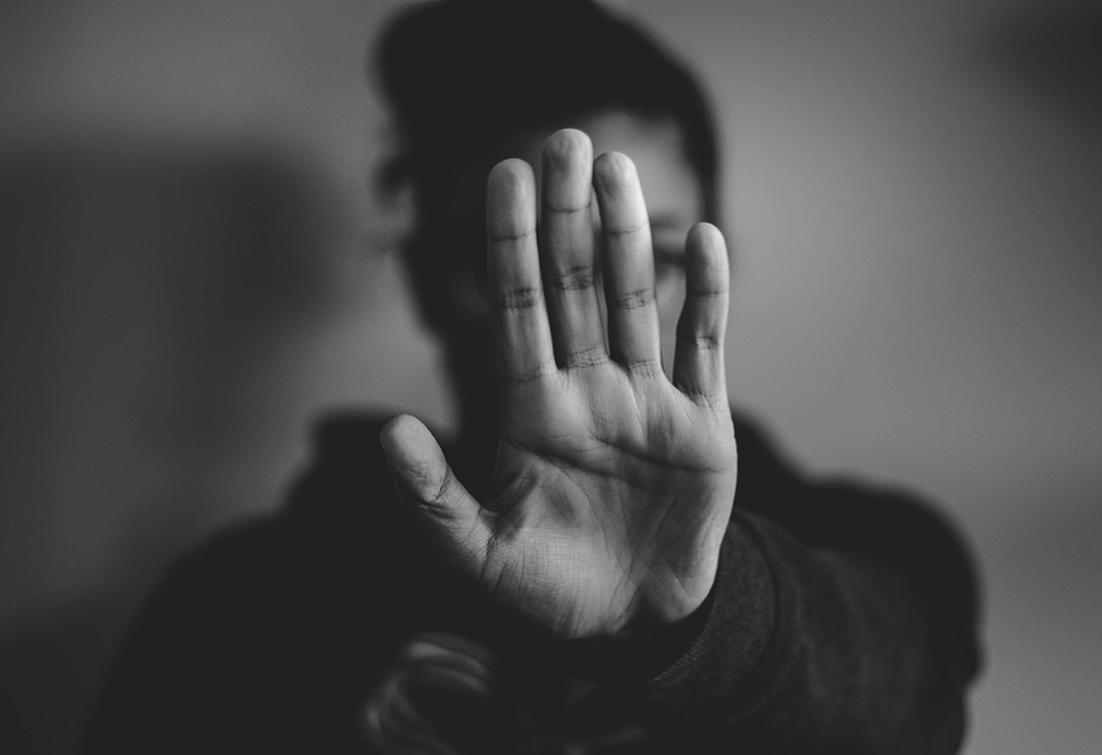 A hand put up in front of a person's face in a gesture of "stop, stay away" (Unsplash/Nadine Shaabana)
