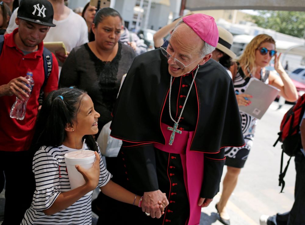 Bishop Mark Seitz of El Paso, Texas, shares a smile with a Honduran girl named Cesia as he walks and prays with a group of migrants at the Lerdo International Bridge in El Paso.